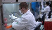 Technician in white coat and mask prepares a DNA sample at a lab bench.