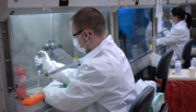 Technician in white coat and mask prepares a DNA sample at a lab bench. 