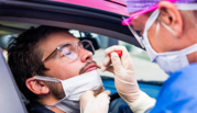 A medical worker administers a COVID-19 nasal swab test to a person in a car. 