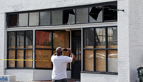 A man facing away takes pictures of a storefront damaged by Tropical Storm Isaias.