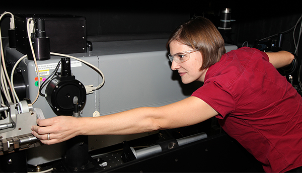 A woman in a red shirt and safety goggles (Catherine Cooksey) reaches along a rectangular gray instrument (RTS).