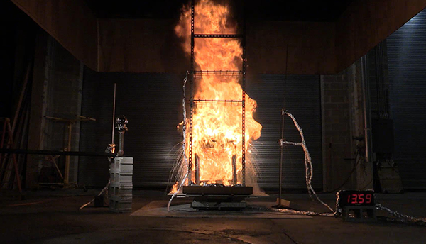 A column of fire rises over a cart structure in a darkened lab.