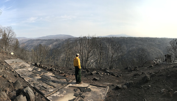 A man (Alexander Maranghides) stands on a hill overlooking a landscape burned by the Camp Fire.