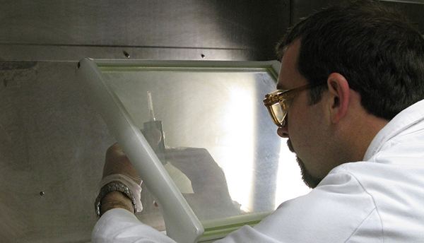 A man (Denis Bergeron) holds a syringe behind a plastic shield. 