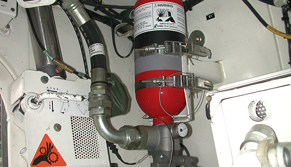 A red fire extinguisher is bolted to the wall of a military vehicle as part of a fire suppression system.