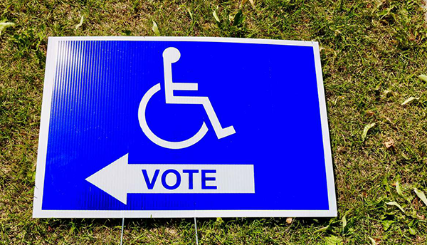 A sign lying in the grass shows an icon of a wheelchair user with an arrow saying "VOTE."