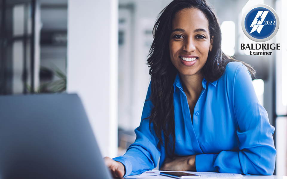 Woman sitting at a desk while leaning on her hand and using her laptop to apply to become a Baldrige examiner.