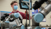 Steven Salisbury works at a computer screen in a lab with robotic arms in the foreground.