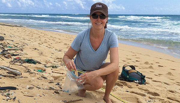 Jennifer Lynch, in a baseball hat and sunglasses, picks up plastic from the beach.