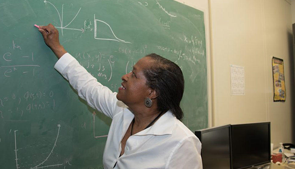 Bonita Saunders reaches up to write math formulas on a chalkboard.