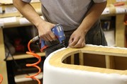 A person attaches foam to wood in an upholstered furniture factory. 