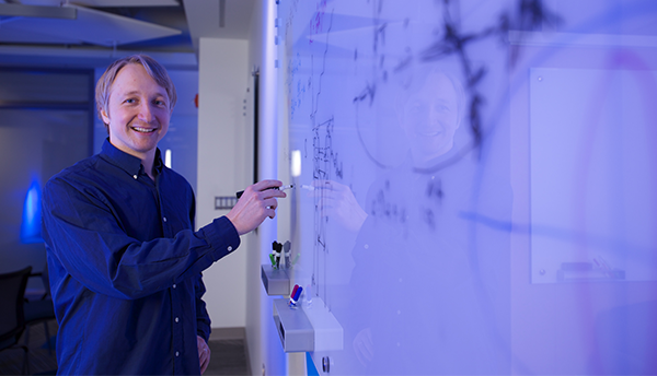 Alexey Gorshkov poses standing at a whiteboard, holding a marker.