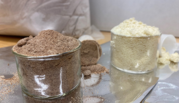 Two open glass containers hold brown flour (left) and white flour, with partially filled plastic scoops lying beside them. 