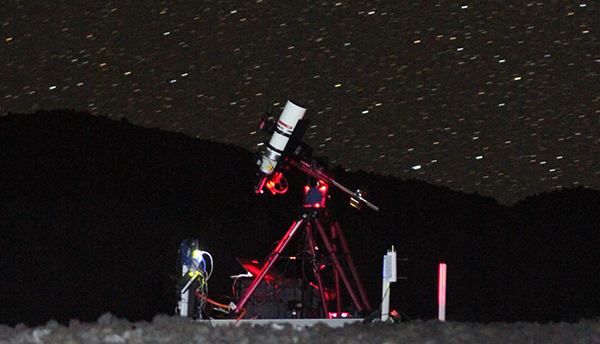 A white telescope on a red scaffolding stands in front of a starry night sky.