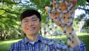 Ming Zheng poses smiling outdoors, holding a model of a carbon nanotube that looks like a large tube made of smaller connecting tubes.
