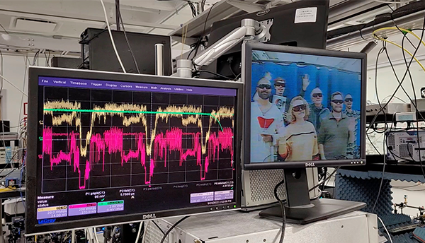 Two monitors side by side show radio waves on the left and waving researchers on the right. 