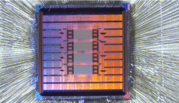 Close-up of a square computer chip with pink and orange metallic shades and four gray rectangles in the center. 