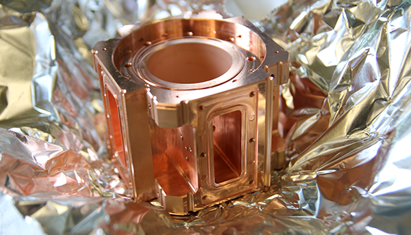 A shiny copper-colored metal device sits on a sheet of crumpled aluminum foil.