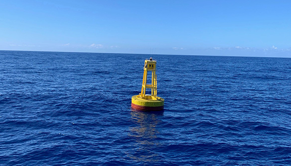A yellow buoy with a red base floats in the sea under a blue sky. 