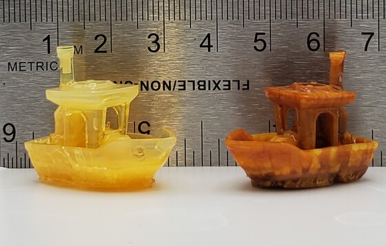 Two tiny plastic boats, yellow and brown, are displayed in front of a ruler.