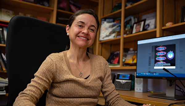 Ana Maria Rey sits at her desk with a computer screen behind her showing physics illustrations.