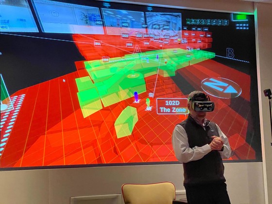 Person wearing VR goggles in front of projection screen showing incident response dashboard