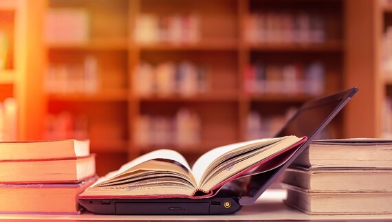 Open laptop and open book next to stacks of books