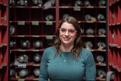 Christina Cecelski, in safety glasses, stands between rows of shelves holding metal cylinders.