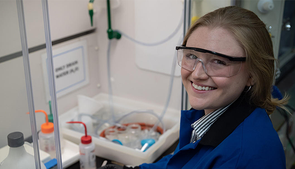 Christine McGinn wears safety glasses as she handles plastic bottles and other materials in the lab. 