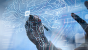 Hands draw on a transparent screen with circuits making the shape of a brain and "AI" written in the center. 