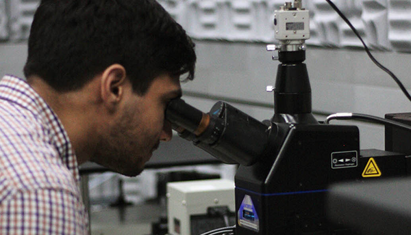 Samuel Márquez González leans forward to look through the eyepiece of a microscope in the lab. 