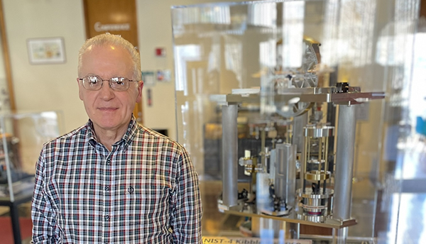 Antonio Possolo stands next to a museum display of a Kibble balance, a complex scientific device.