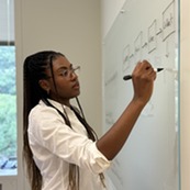 Ashley Hartwell stands at a whiteboard, writing with a marker. 