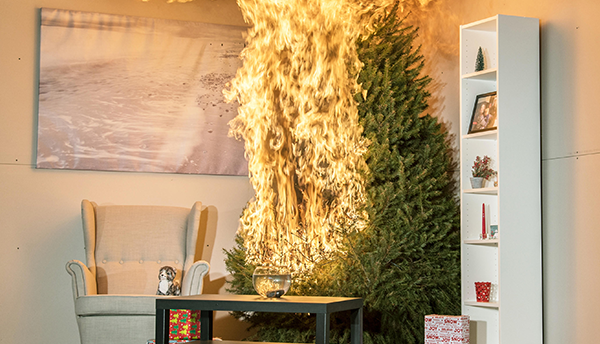 Flames are devouring one side of a Christmas tree in a staged living-room scene inside a fire lab.