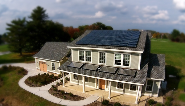 The two-story net-zero house has an attached garage and solar panels on the roof.