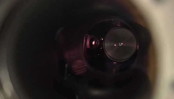 Rydberg atom thermometer: View through a circular opening into a dark interior. A red dot floats in the darkness. 