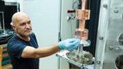 Vladislav Gerginov wearing latex gloves reaches out to adjust something on a cylindrical metal scientific device for NIST-F4.