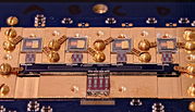 Circuit board with various square chips and gold screws. Small letters in the center say: NIST True Bq.