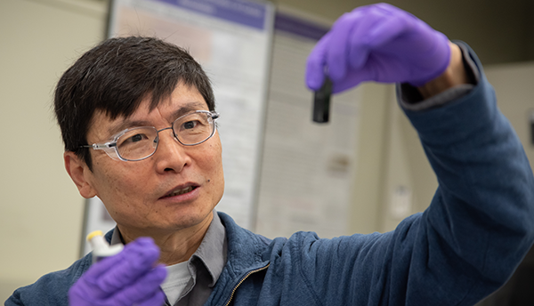 Researcher Ming Zheng looks with interest at a small vial he is holding up in front of him. 
