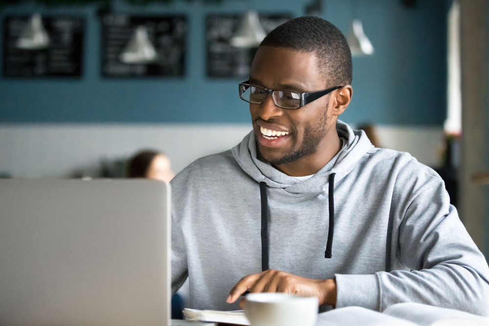 smiling man sitting in a coffee shop looking at a laptop computer