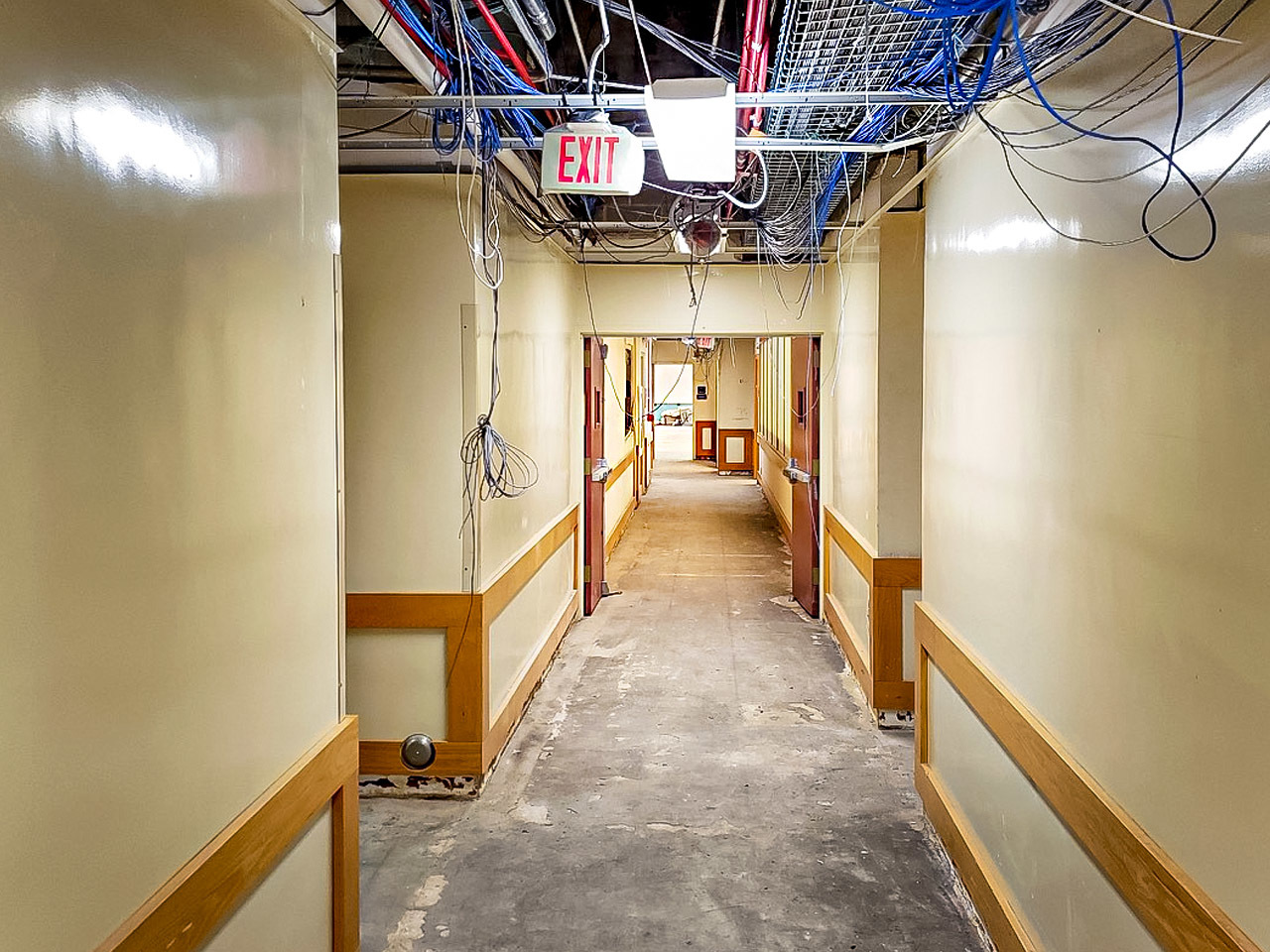 Photo of asbestos abatement of 1st floor and mezzanine of NLM Building 38. Hallway with hanging wires from open ceiling is shown.
