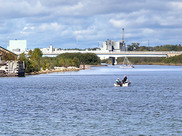 Anglers fish on a boat in the Manistique River, with urban development in the background.