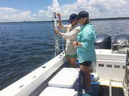 Two scientists on a boat monitor ocean waters with an approximately two-foot long, tube-like device.