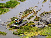 Aerial view of a large excavator working in a natural wetland environment in Louisiana.