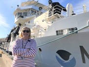 A NOAA scientists poses in front of the hull of the NOAA research vessel, Reuben Lasker.