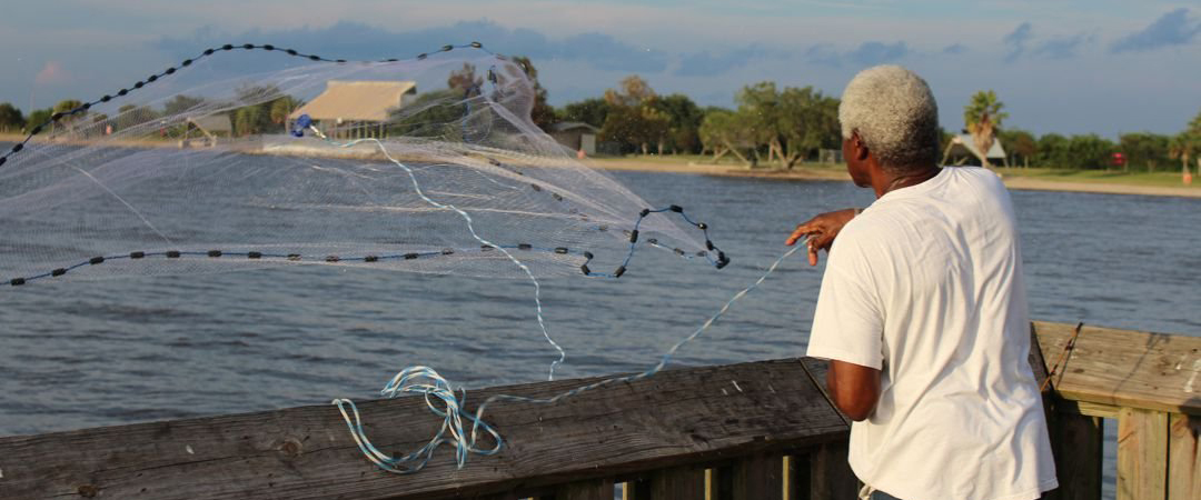 A recreational angler tosses a net out off a fishing pier.
