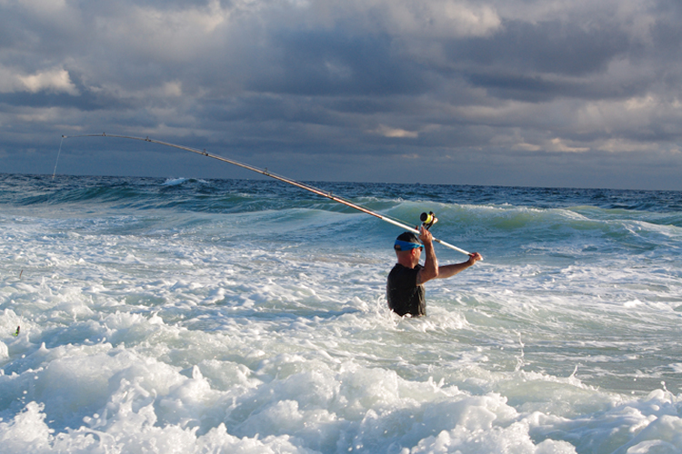An angler casts a line in the surf.