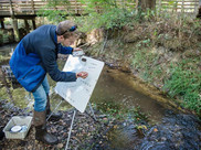 A teacher adds data to a graph on a posterboard by a stream.