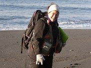 Award winner Dr. Anne Shaffer walks on a beach with a backpack, clipboard and other scientific equipment.