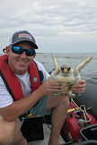 Jason Letort on a small boat, holding a juvenile loggerhead sea turtle. 